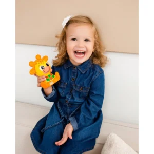 Smiling toddler in a denim dress holding a yellow sun-shaped toy giraffe with an orange mane.