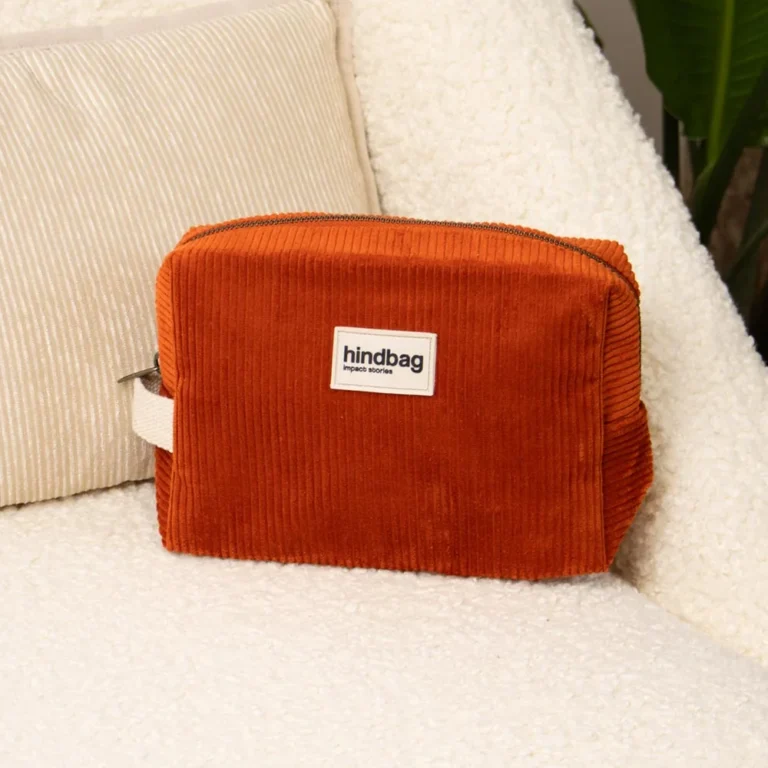 Orange corduroy zip pouch with a white hindbag brand label, placed on a fluffy white surface.
