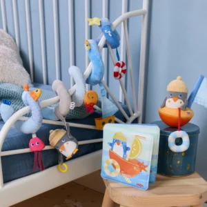 Blue-themed children's bed with hanging plush sea creatures and a penguin figure by a nautical storage box and book clubbed on a stool.