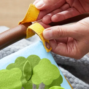 Person fastening a yellow Velcro strap around a limb, securing a strap while a colorful toy with green trees is nearby
