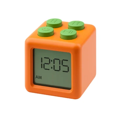 Orange cube-shaped toy clock with four green LEGO-style studs on top and a digital display showing 12:05 AM