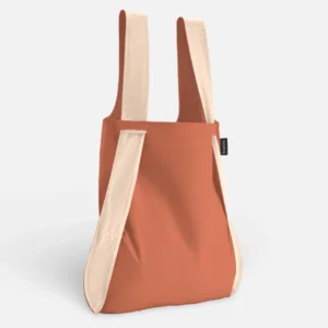 Rust-orange tote bag with wide cream straps and a small brand tag on the side, standing upright.